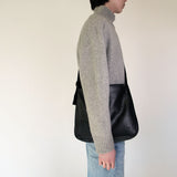 Person wearing a gray sweater and NImes black messenger bag on a plain background
