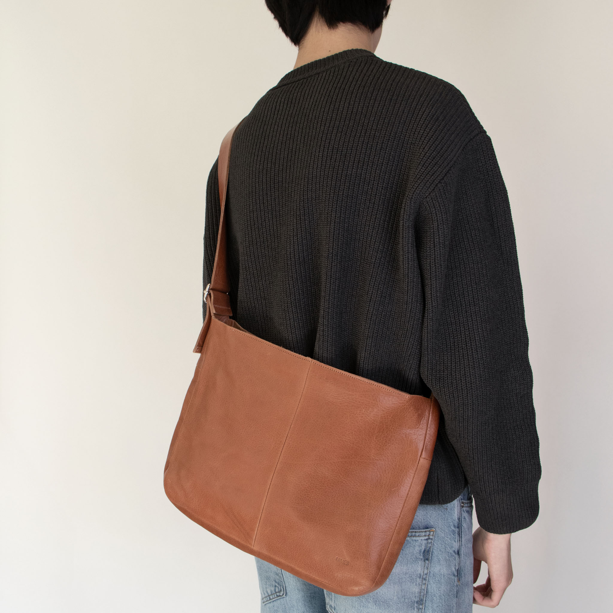 Person wearing a dark gray sweater and NImes tobacco messenger bag on a plain background
