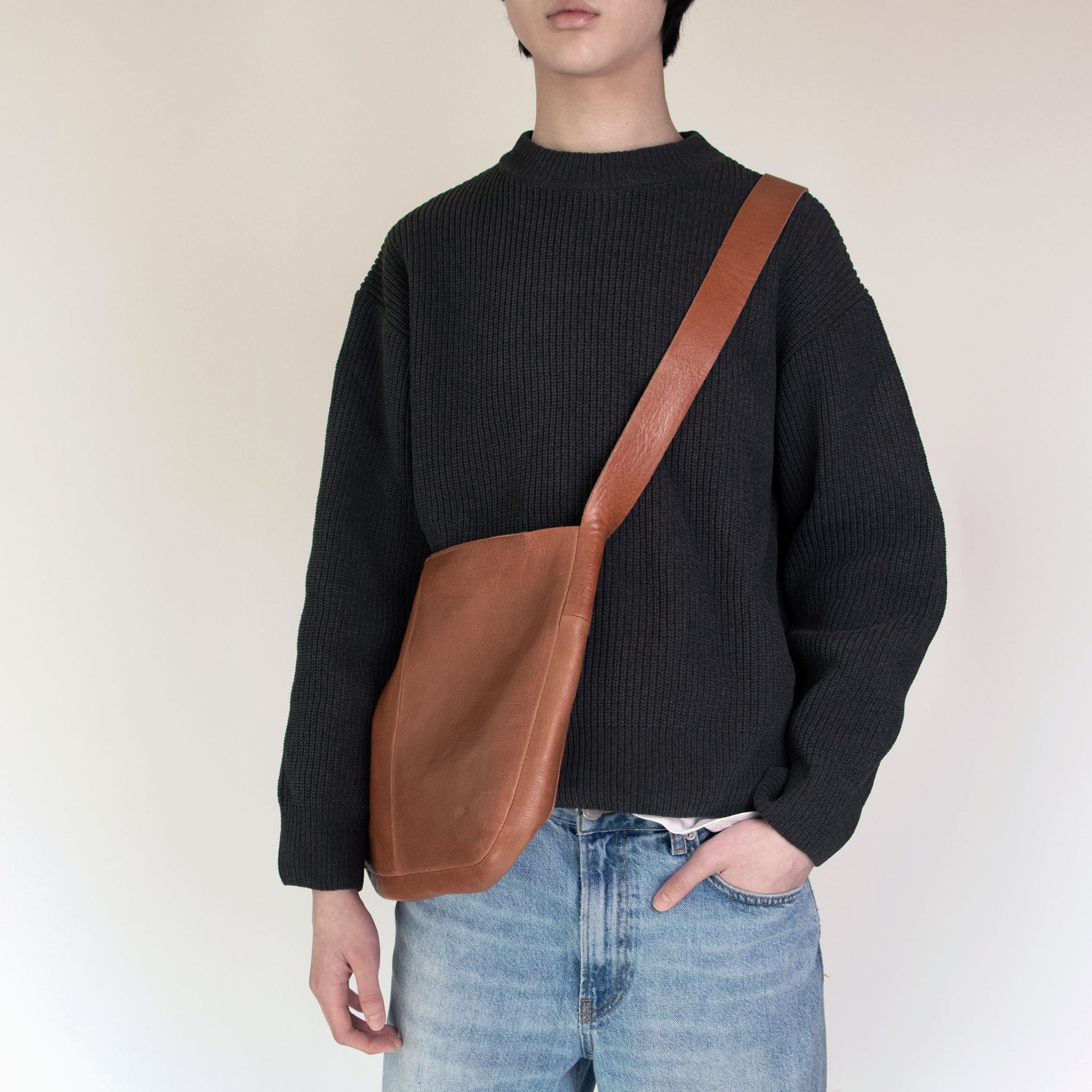 Person wearing a dark gray sweater and NImes tobacco messenger bag on a plain background