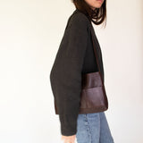 Person wearing a dark gray sweater and jeans carrying Nimes mini bonarda in dark brown  on a light background