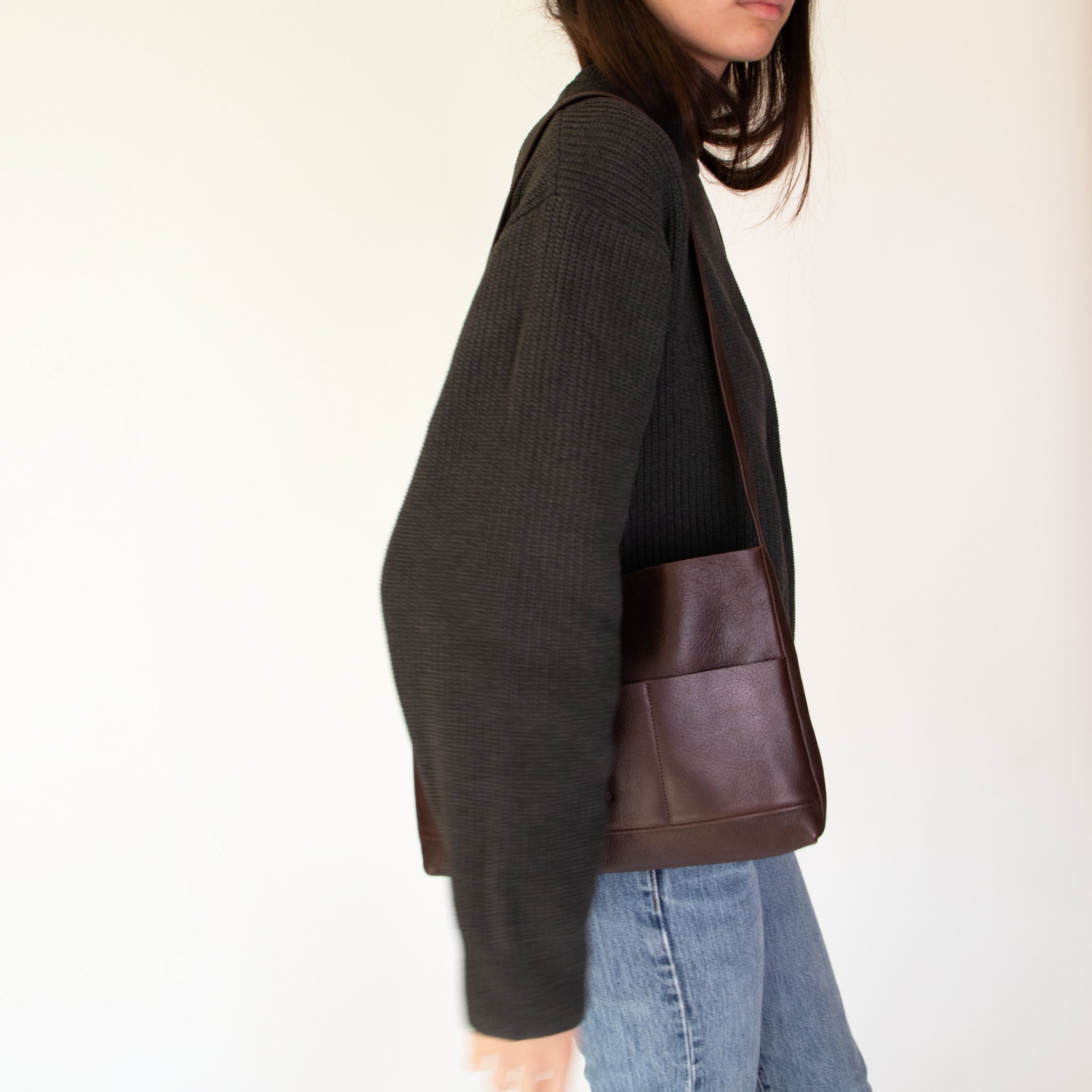 Person wearing a dark gray sweater and jeans carrying Nimes mini bonarda in dark brown  on a light background