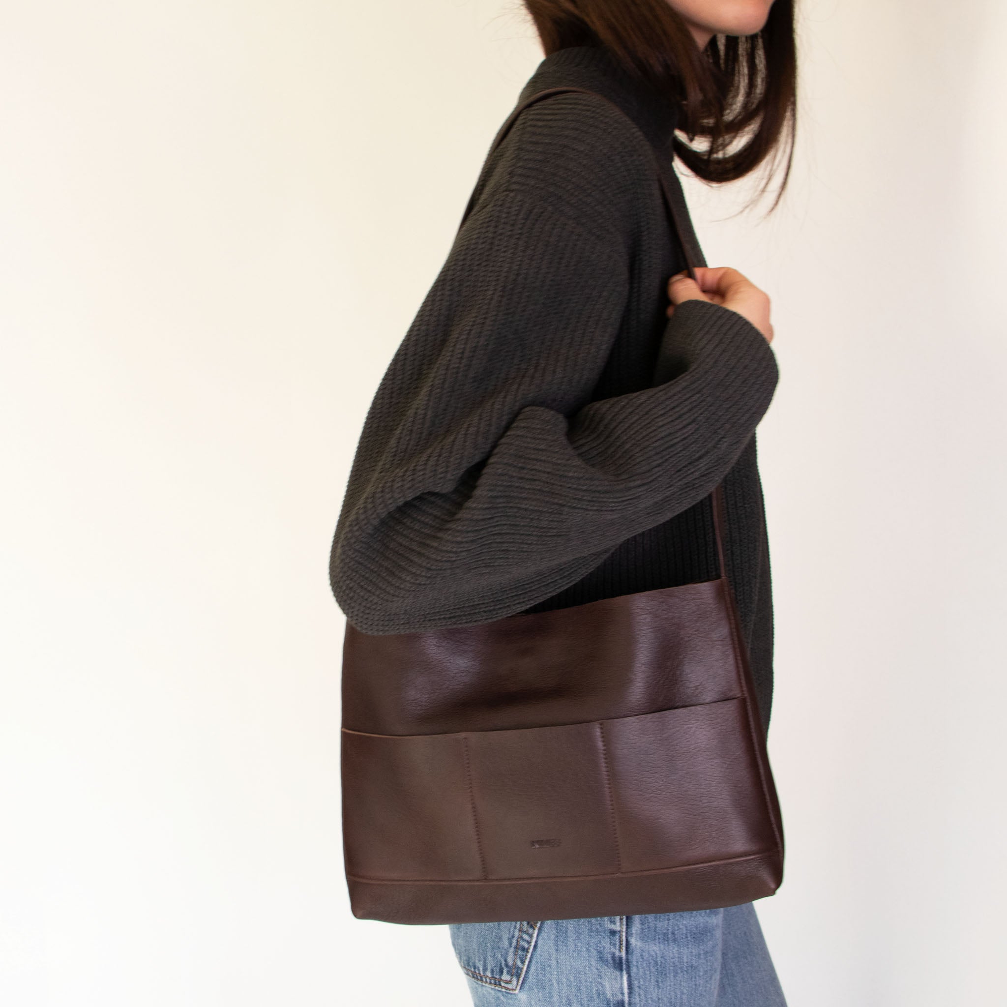 Person wearing a dark gray sweater and jeans carrying Nimes mini bonarda in dark brown  on a light background