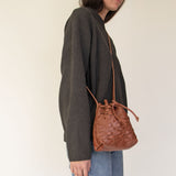 Person wearing a dark gray sweater and NImes weave bucket bag on a plain background