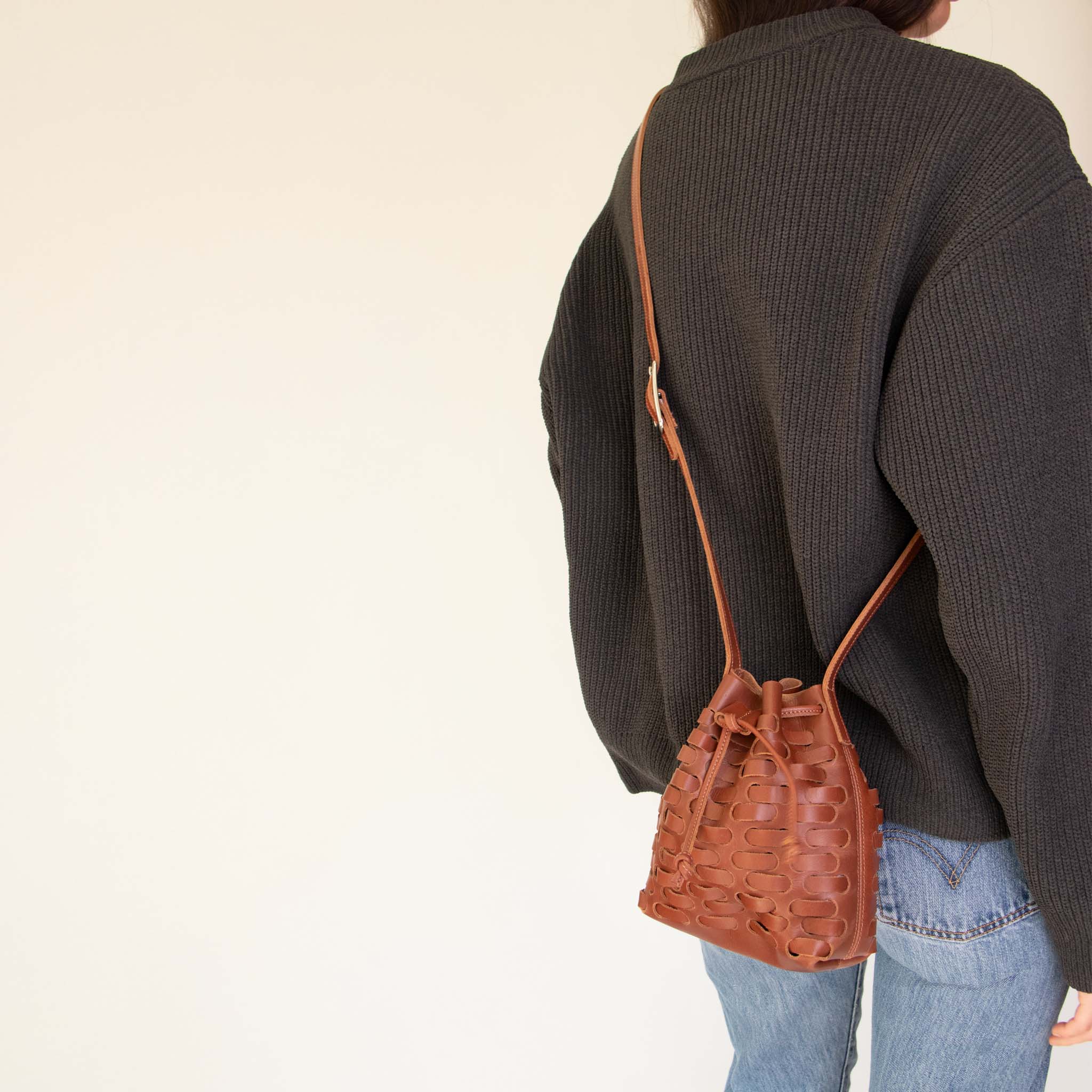 Person wearing a dark gray sweater and NImes weave bucket bag on a plain background
