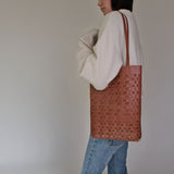 Person wearing a white sweater and NImes weave tote bag in tobacco on a plain background