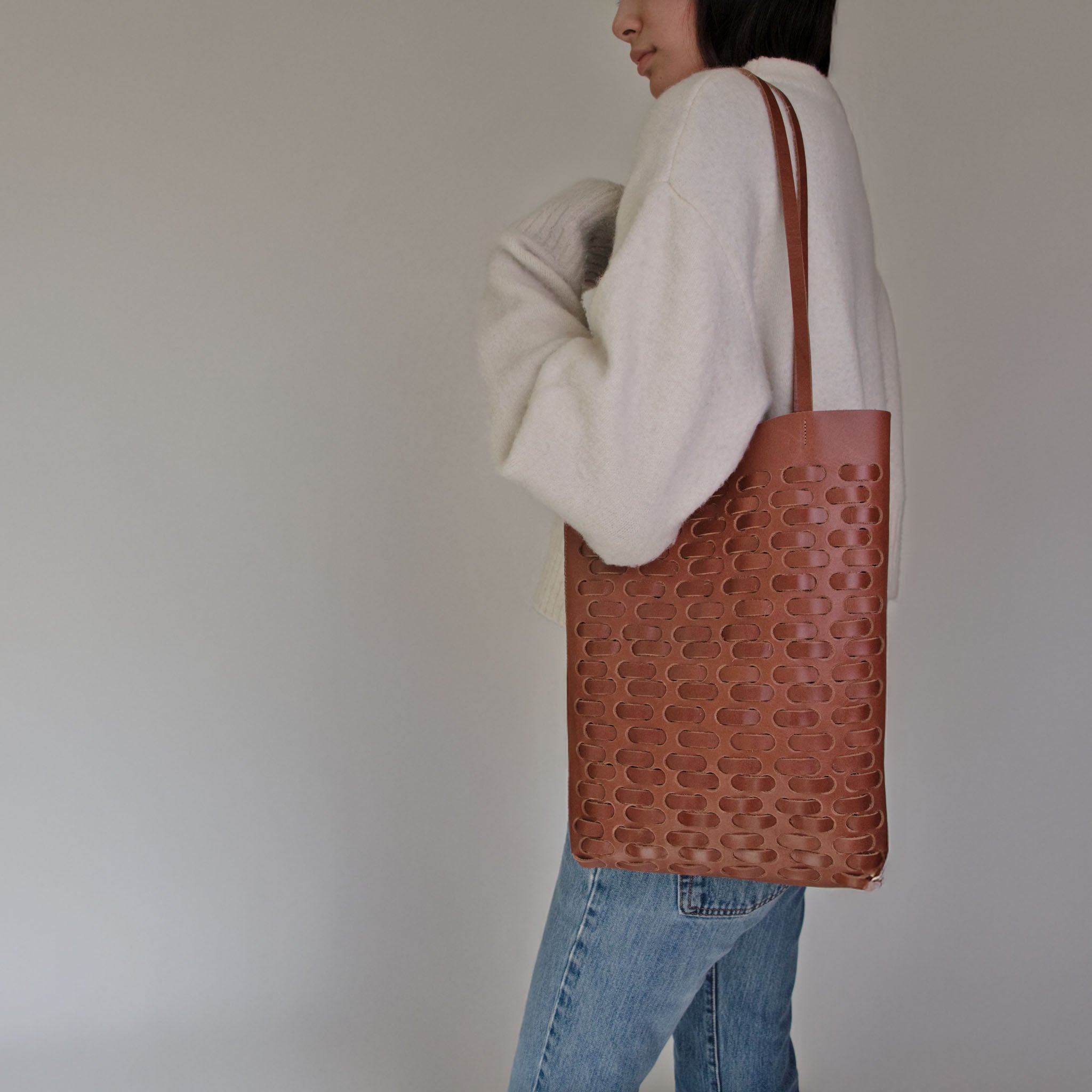 Person wearing a white sweater and NImes weave tote bag in tobacco on a plain background