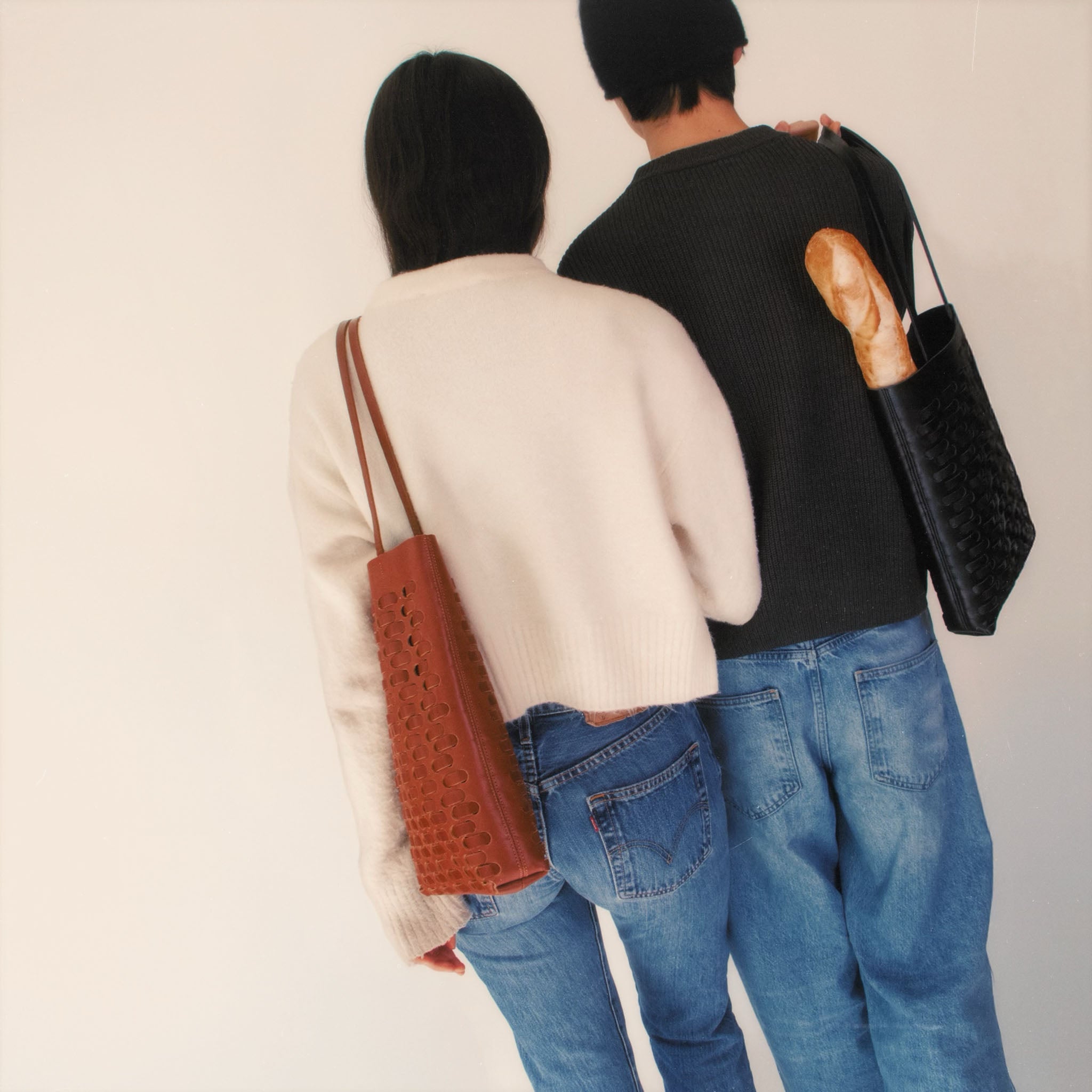 A couple wearing sweathers and jeans both carryng the Nimes woven tote in black and tobacco