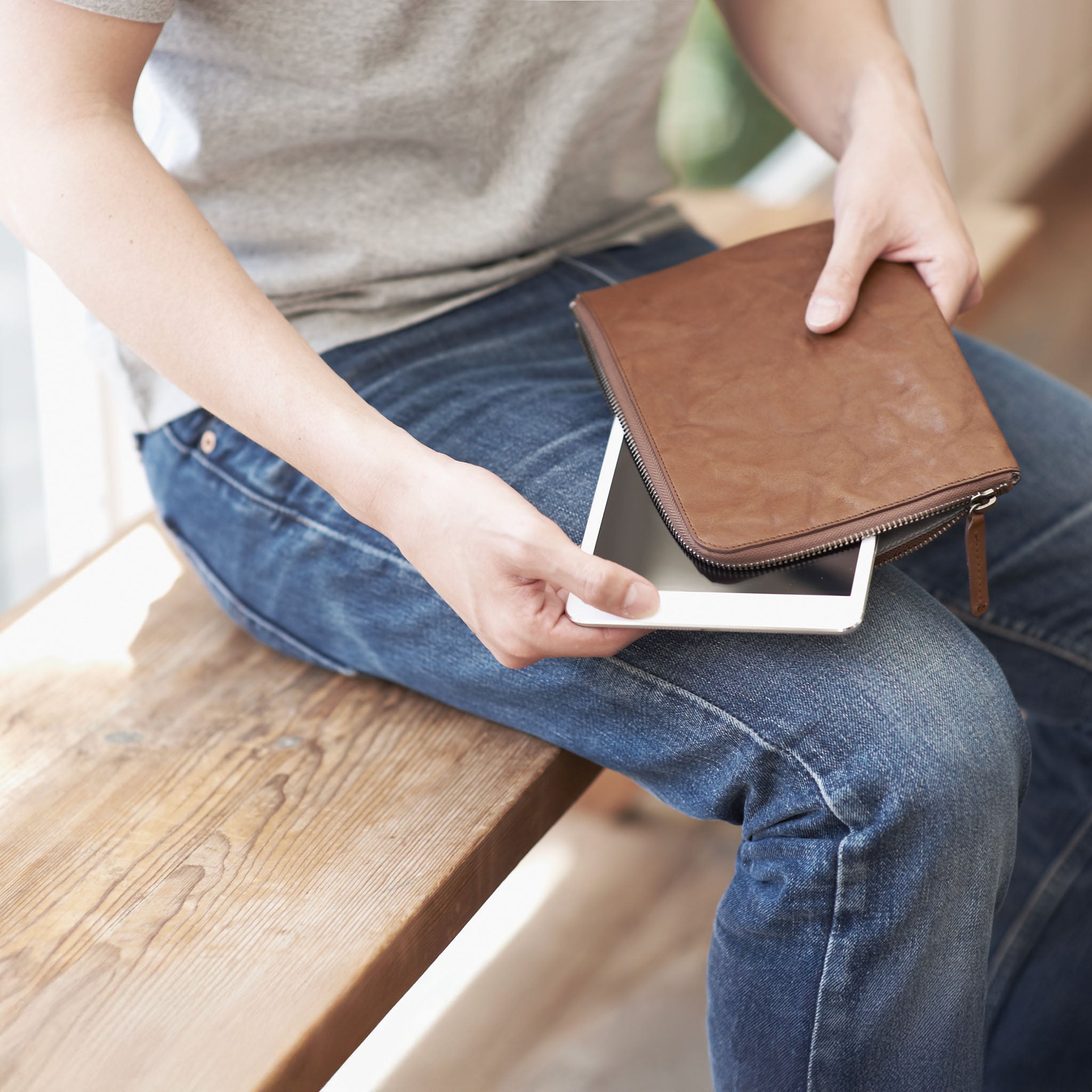 Person sitting on a wooden bench holding a hmny's brown 10 mile bag and pulling out a white tablet