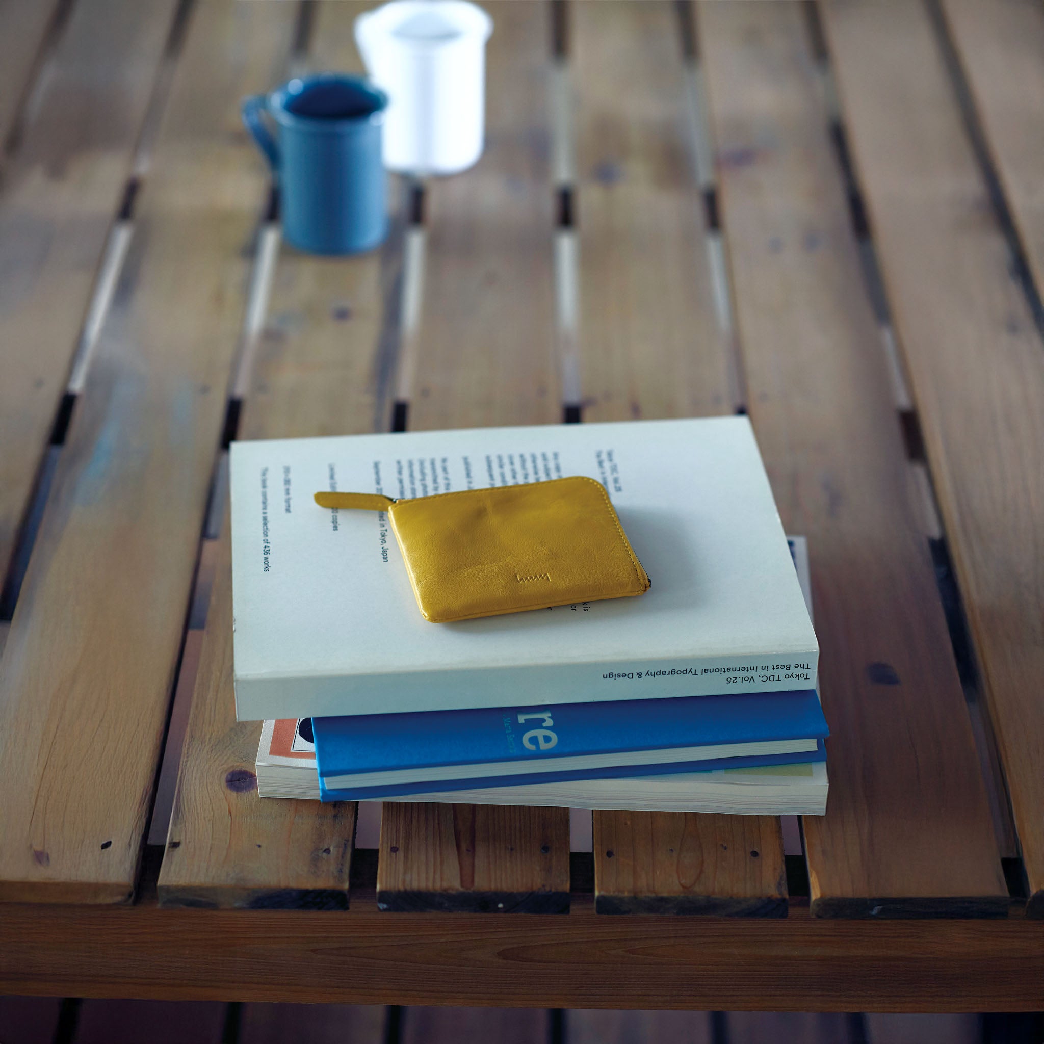 Stack of books with hmny's yellow compact yellow wallet on a wooden table