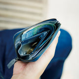 Hand holding an open hmny navy compact wallet with money and cards against a blurred background