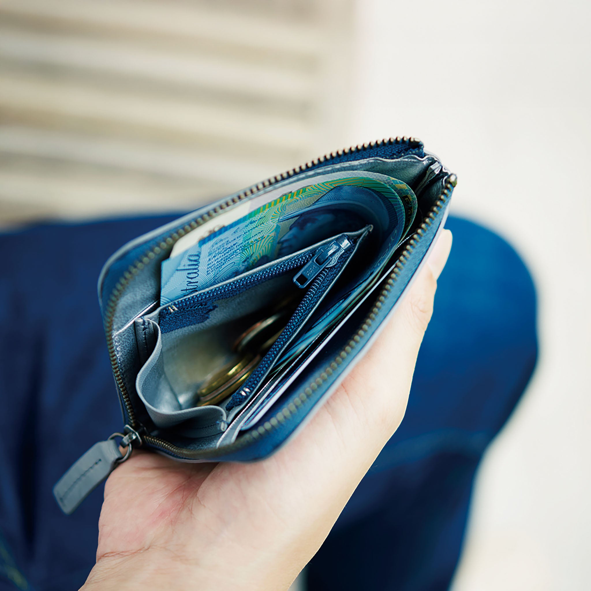 Hand holding an open hmny navy compact wallet with money and cards against a blurred background