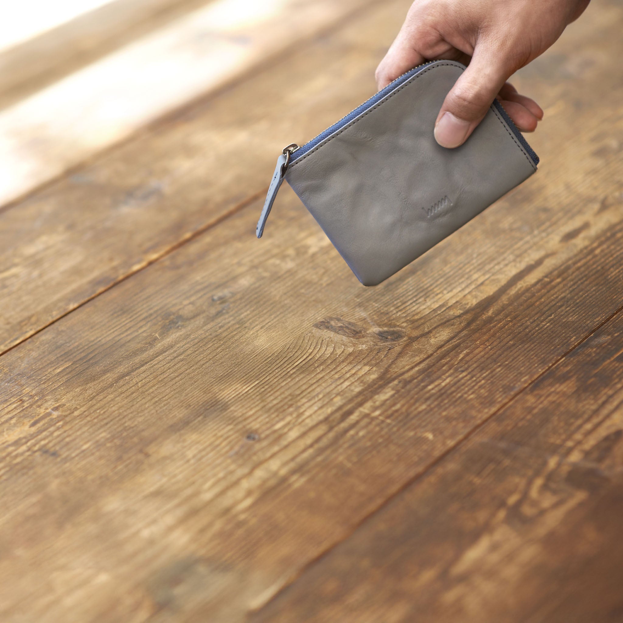 hmny's gray compact wallet held by a hand on a wooden surface