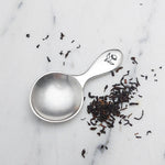 lifestyle image of beehive pewter tea scoop next to tea leaves