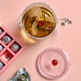 Tea with floral elements in a glass mug, pink chocolates, and a pink coaster on a pink background