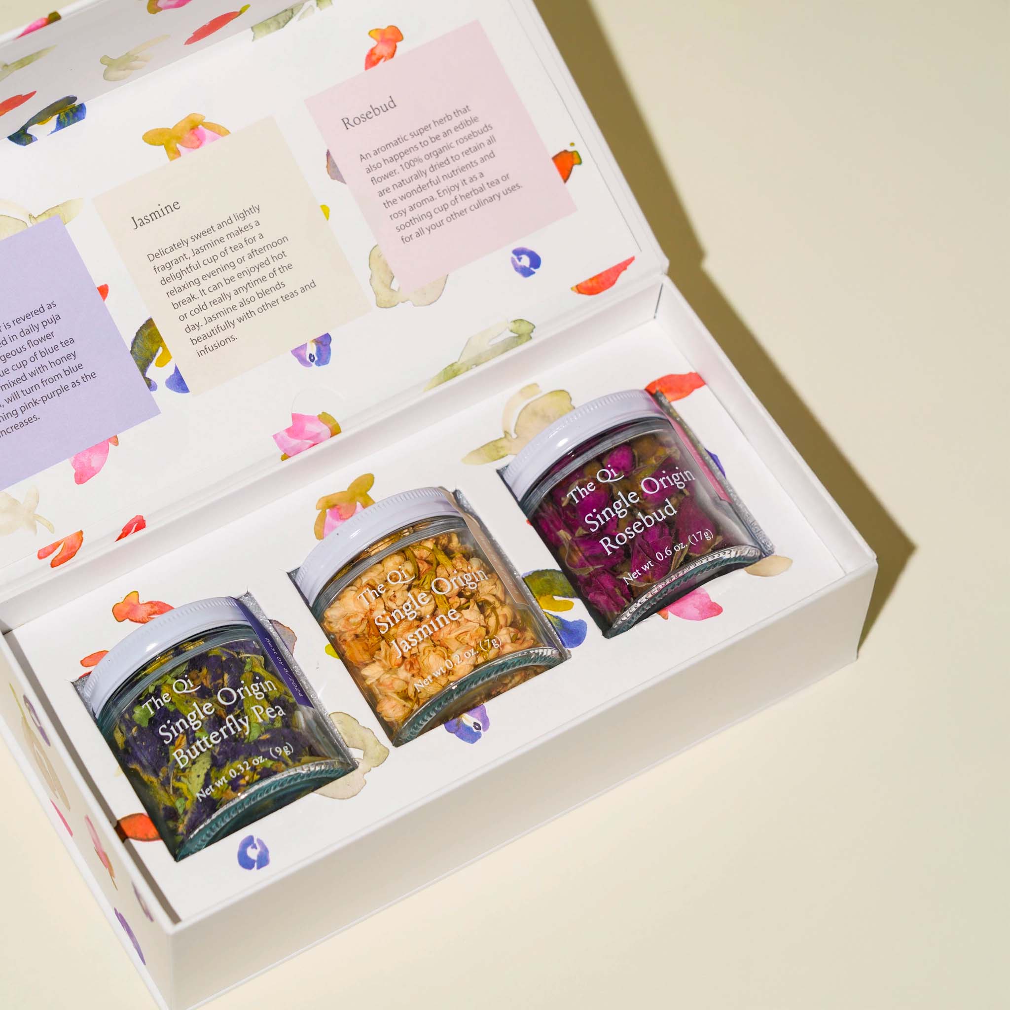 Three small jars of floral tea in a decorative box with colorful labels.