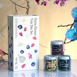 Tea set with 'Petite Flower' packaging and three jars of tea on a reflective surface with floral decorations.