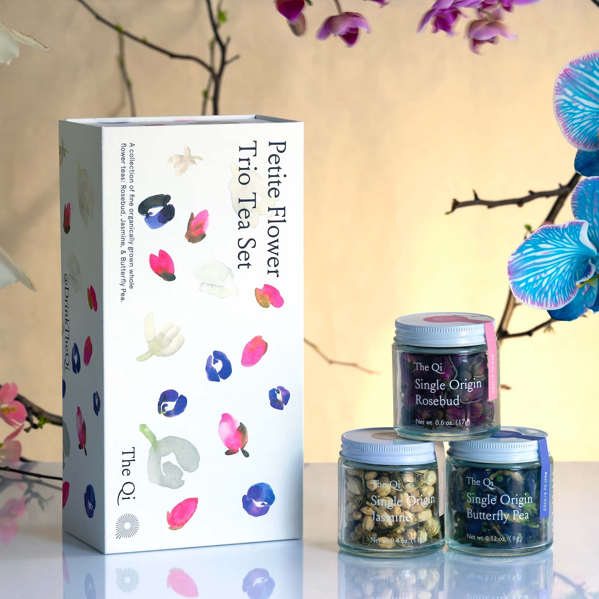 Tea set with 'Petite Flower' packaging and three jars of tea on a reflective surface with floral decorations.