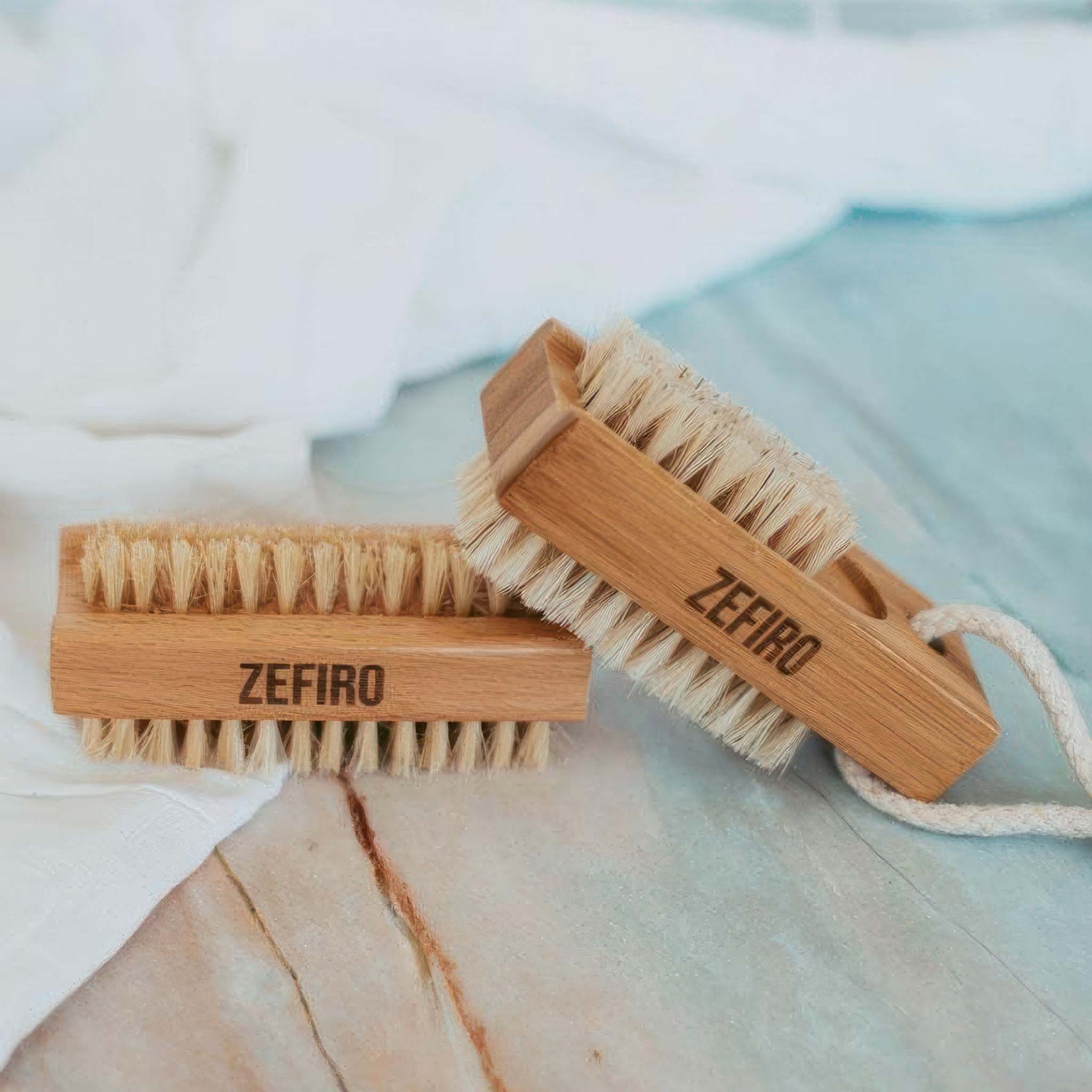 Two wooden nail brushes with bristle heads on a textured surface, branded 'Zefiro'.