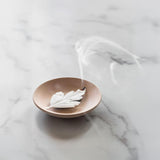 Ceramic incense holder burning a leaf incense with white smoke on a marble surface