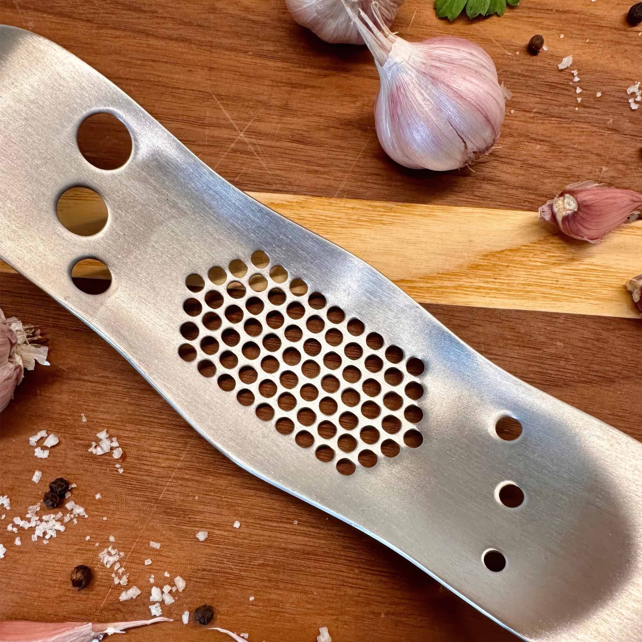 Metal garlic press on a wooden surface with garlic and salt around