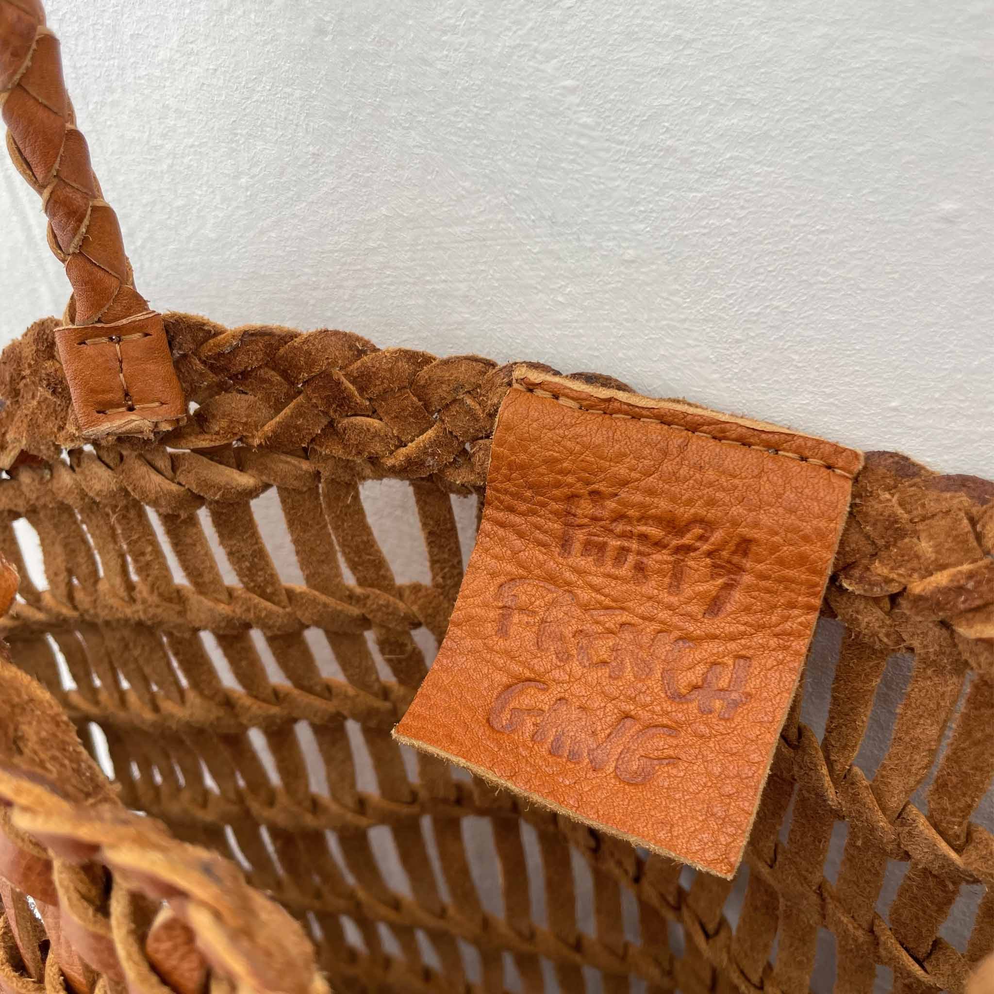 Close-up of a woven brown woven leather bag with a brand label on a white background