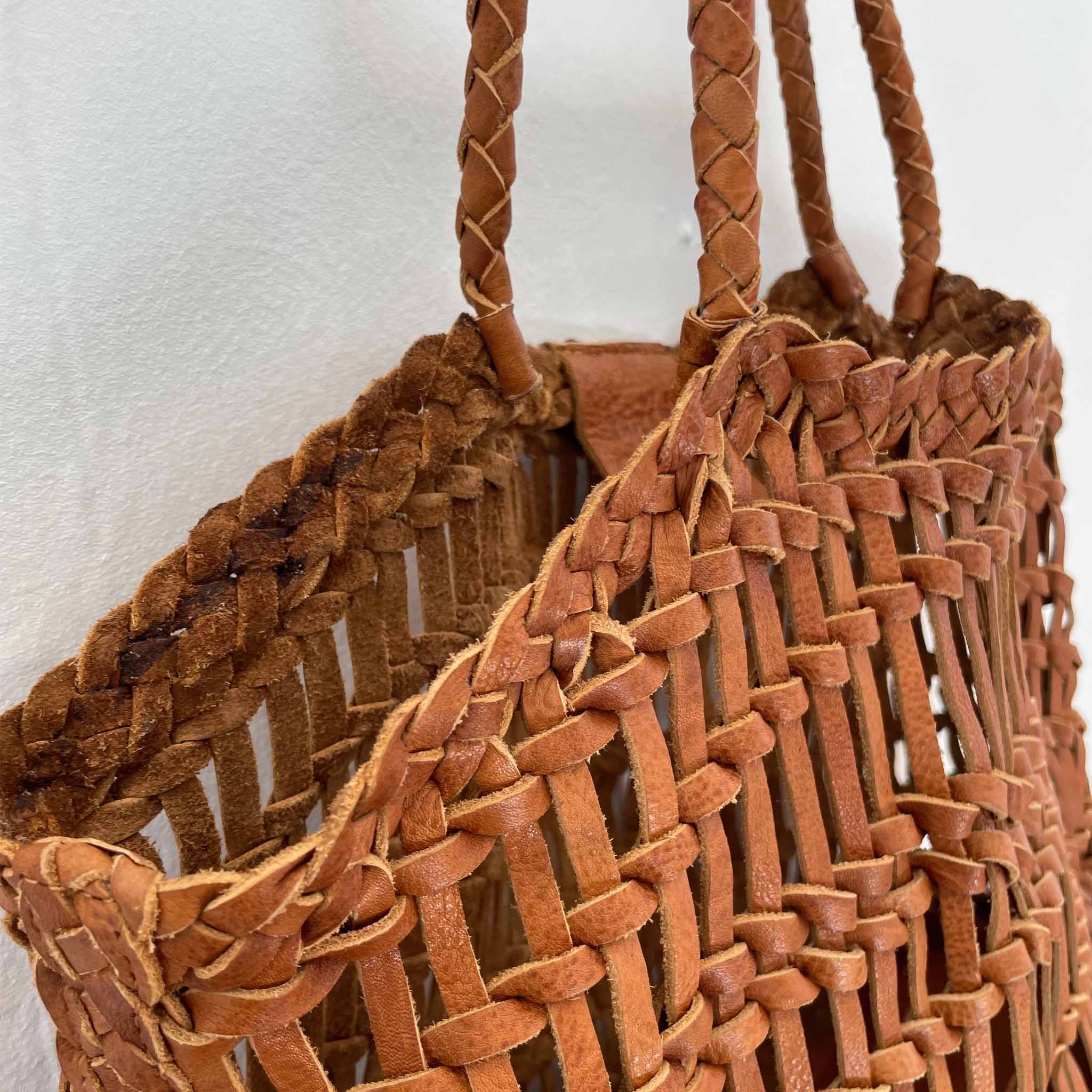 Close-up of a woven brown leather handbag with braided handles on a white background