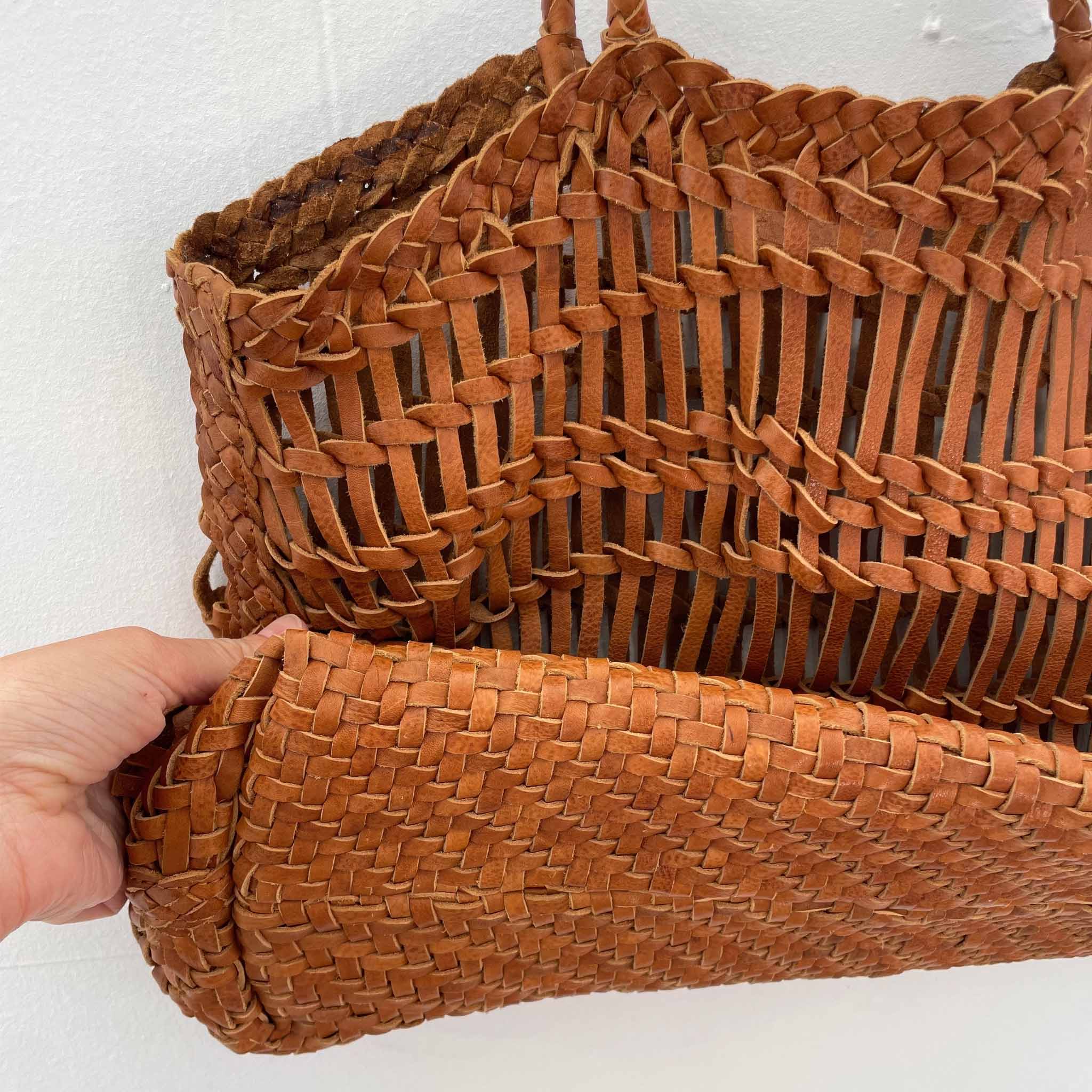 Brown woven handbag held by a hand showing the base weave against a white background