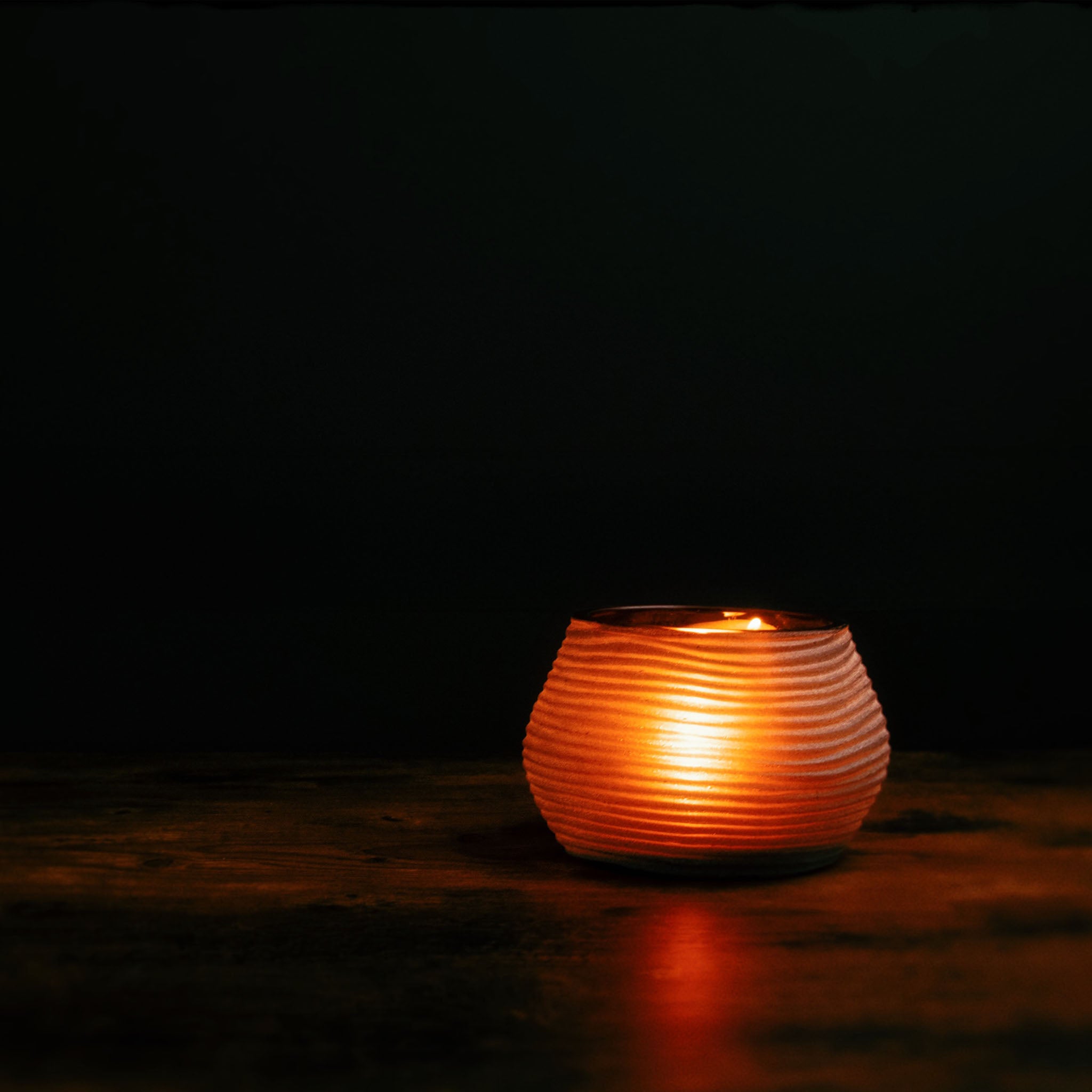 Image of a lit tea light candle inside a candle holder by Nordhaven on a dark background