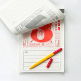 Japanese wall calendar flipped to a day with red lettering and a pen