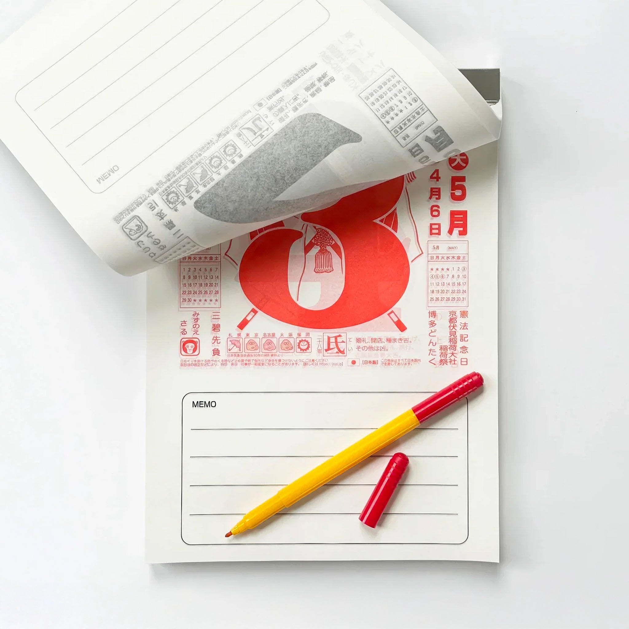 Japanese wall calendar flipped to a day with red lettering and a pen