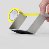 Person tilting the Multi Radius Tape Dispenser that is holding a roll of yellow tape