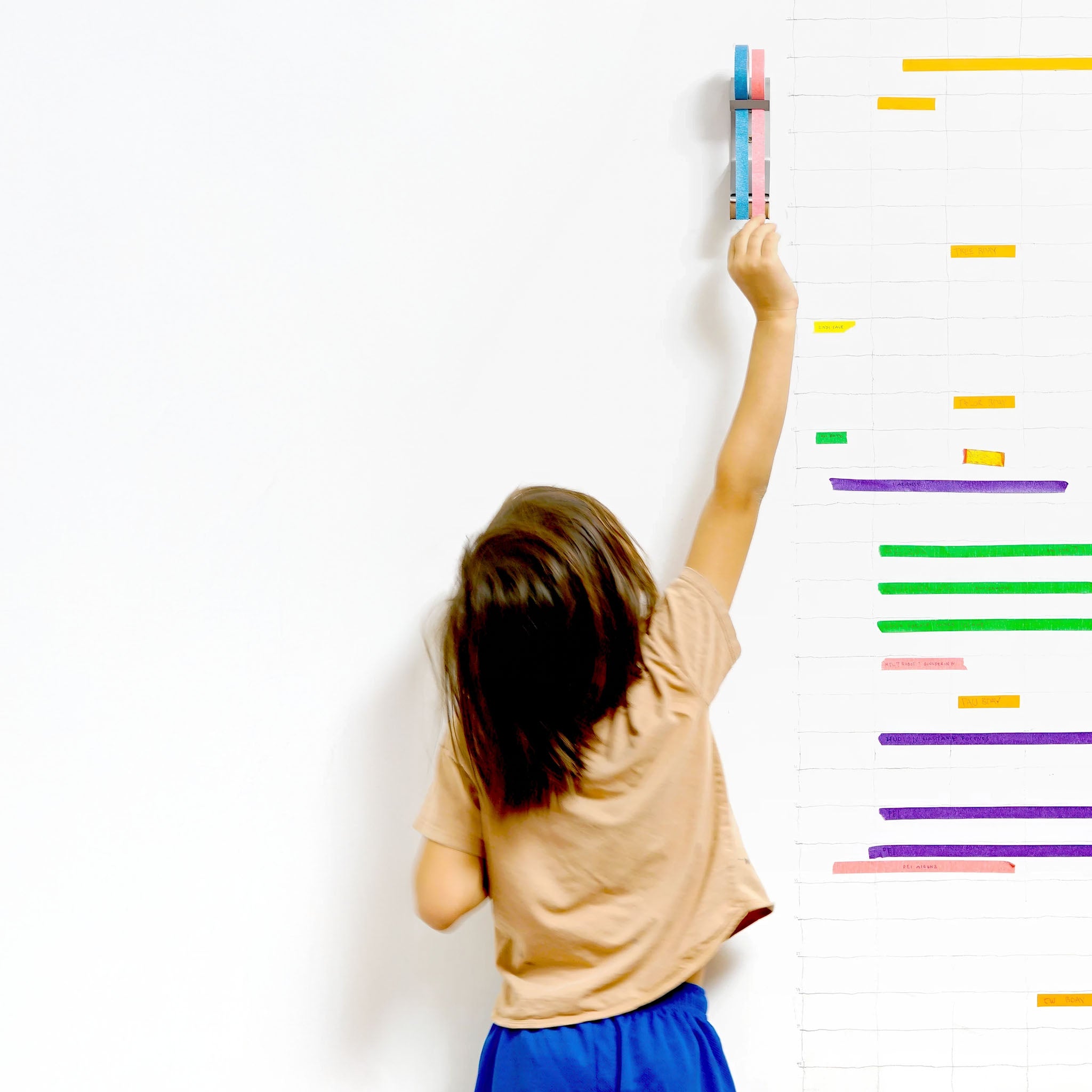 A child reaching up to get a piece of tape that is mounted on a a white wall
