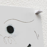 Closeup of a white ninja mini pin holding up a drawing on a white cork board