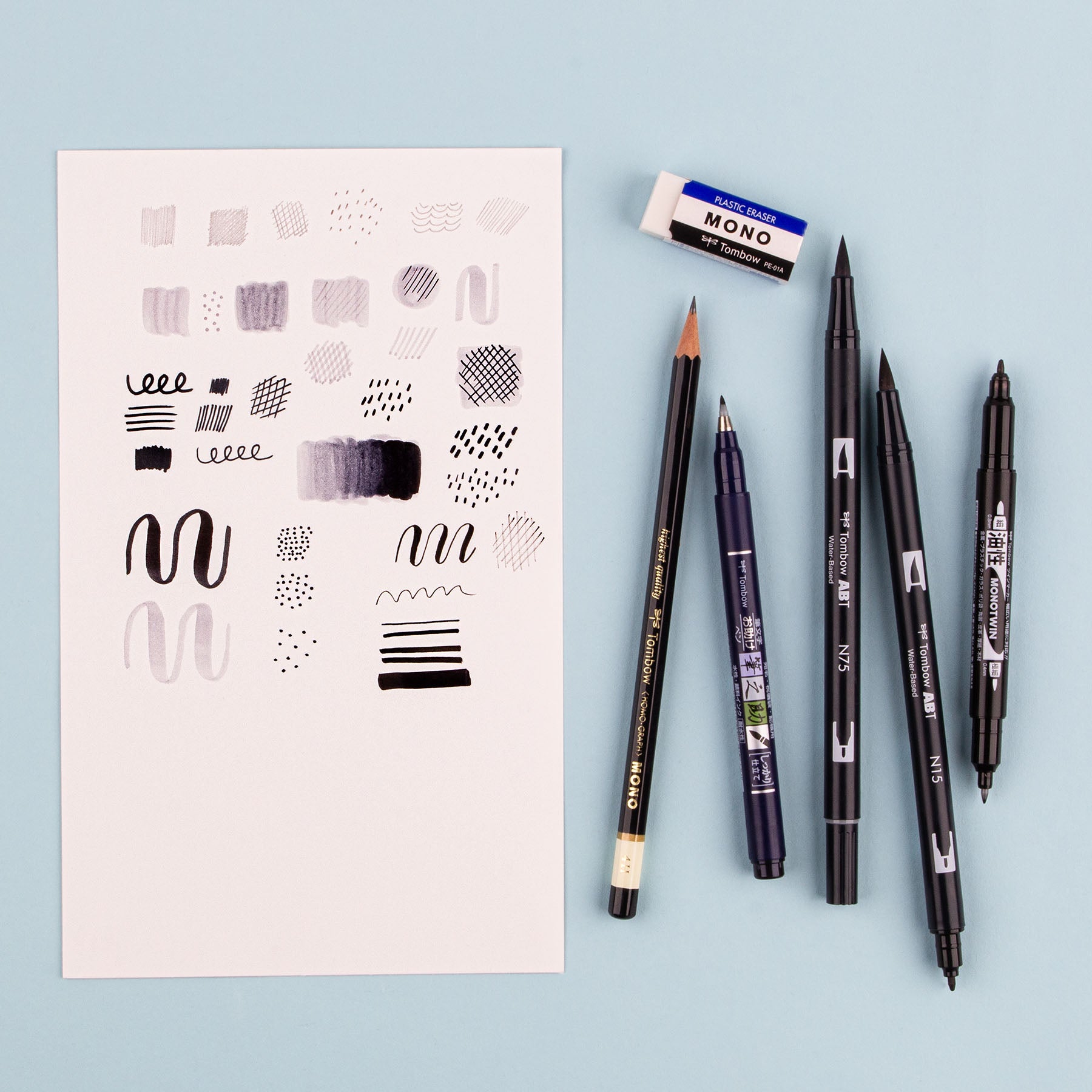 Set of drawing tools including pens and a notebook with patterns on a light blue background