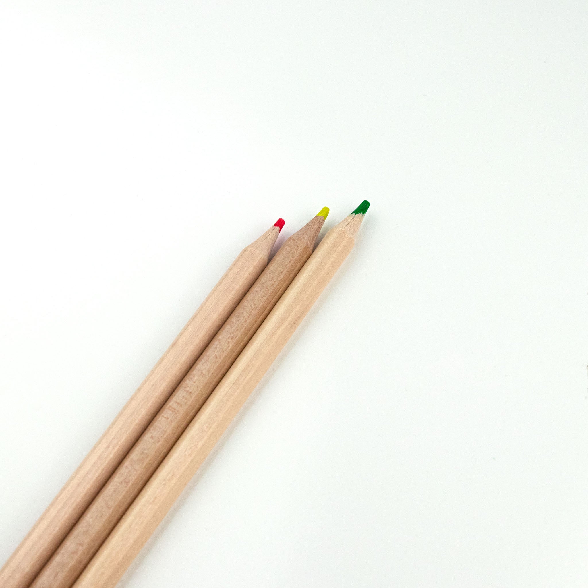 Three highlighter pencils with wooden bodies and colorful tips on a white background