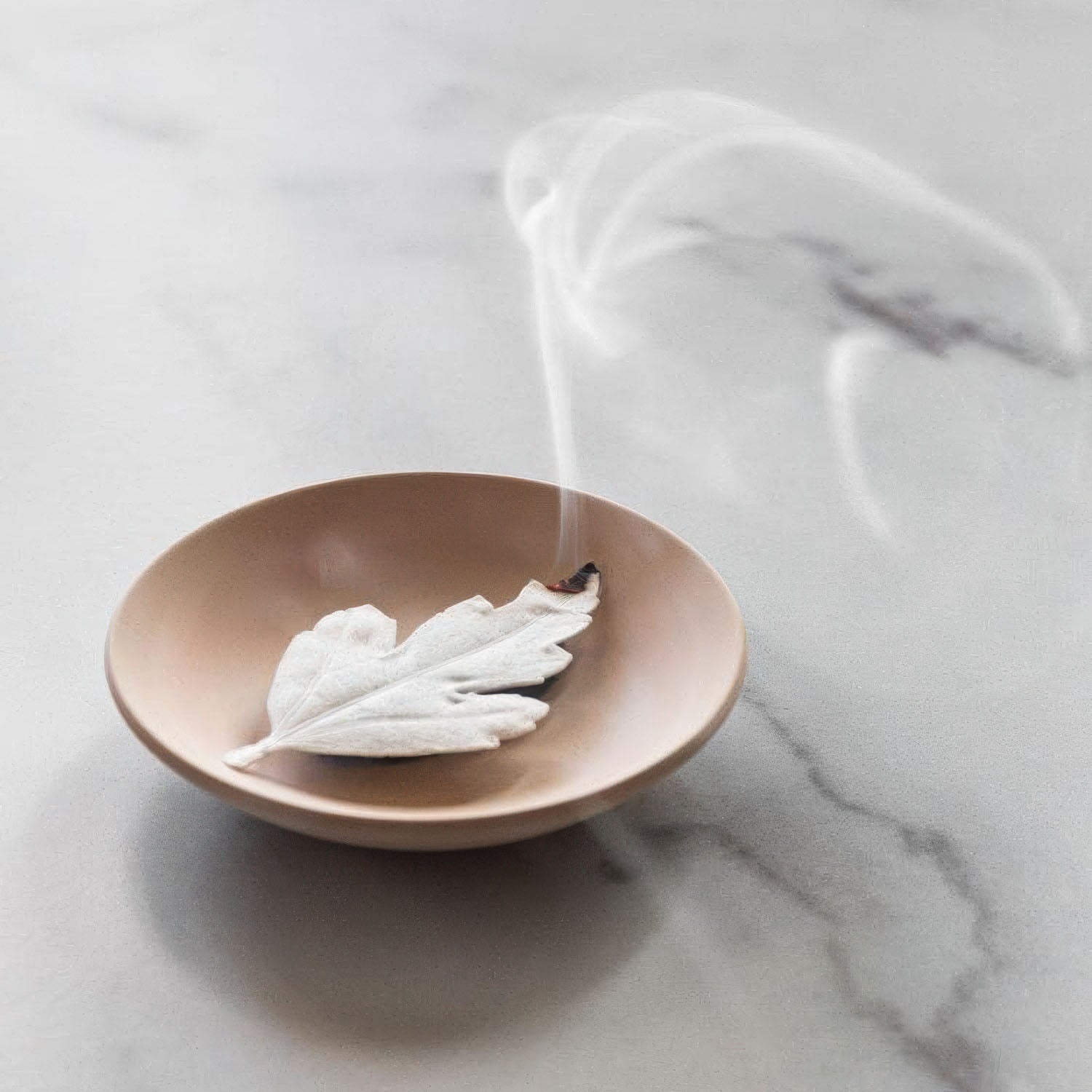 Incense paper leaf burning in a wooden bowl on a marble surface