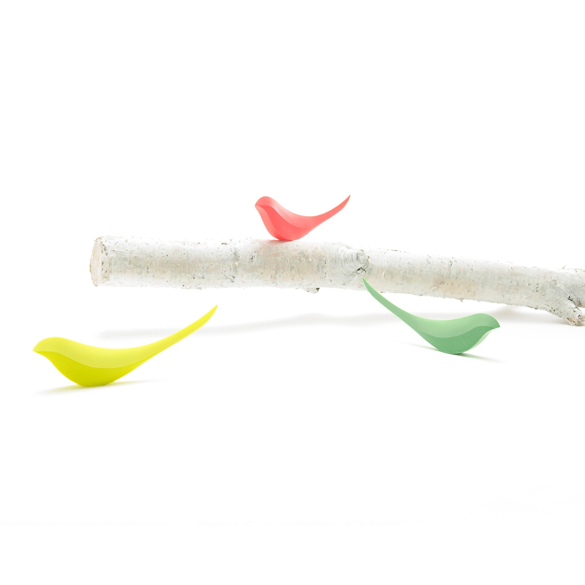 Colorful bird-shaped letter openers on a white branch against a white background