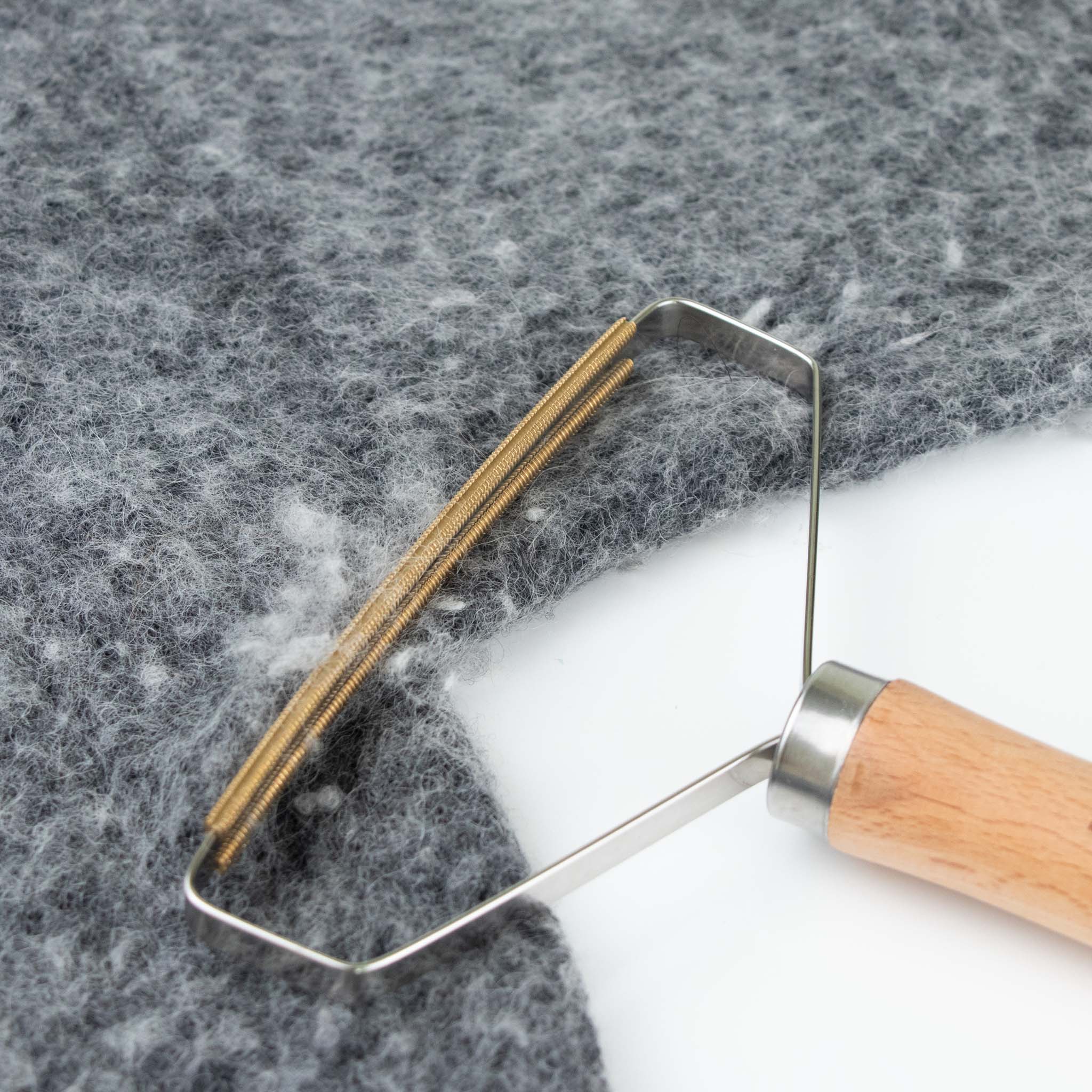 Image of the Beechwood stainless steel and copper lint remover removing lint from a grey sweater