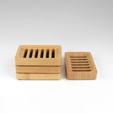 Stack of rectangular wooden soap dishes with slotted drainage design, shown in natural wood tone with one dish displayed separately on a white background.