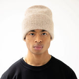 Model wearing an iced taupe knit beanie and black sleeveless top on a white background