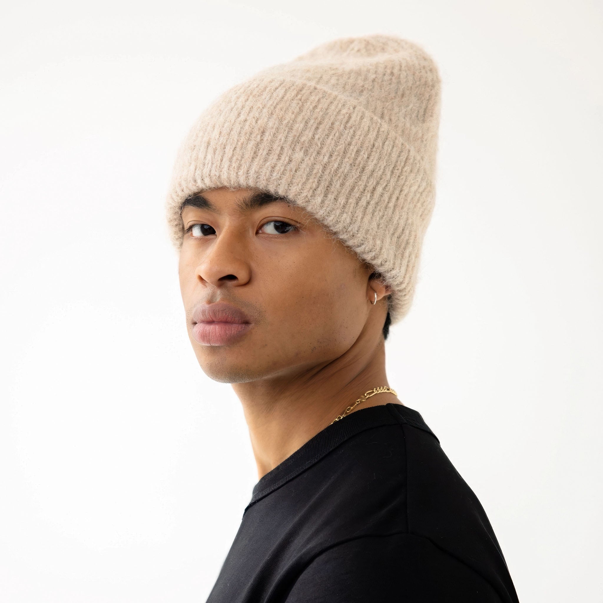Model wearing an iced taupe knit beanie and black sleeveless top on a white background