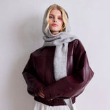 Person wearing a burgundy leather jacket and gray hooded scarf against a plain background