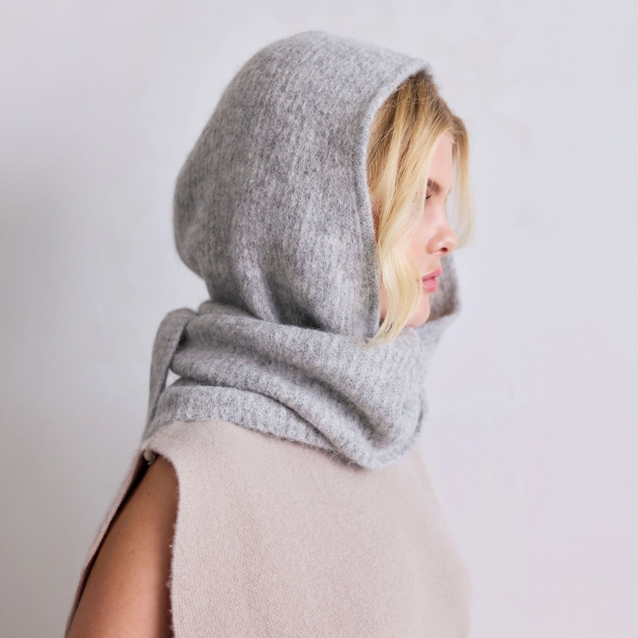Person wearing a gray hooded knit scarf on a light background