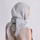 Person wearing a gray hooded knit scarf with a bow on a plain background