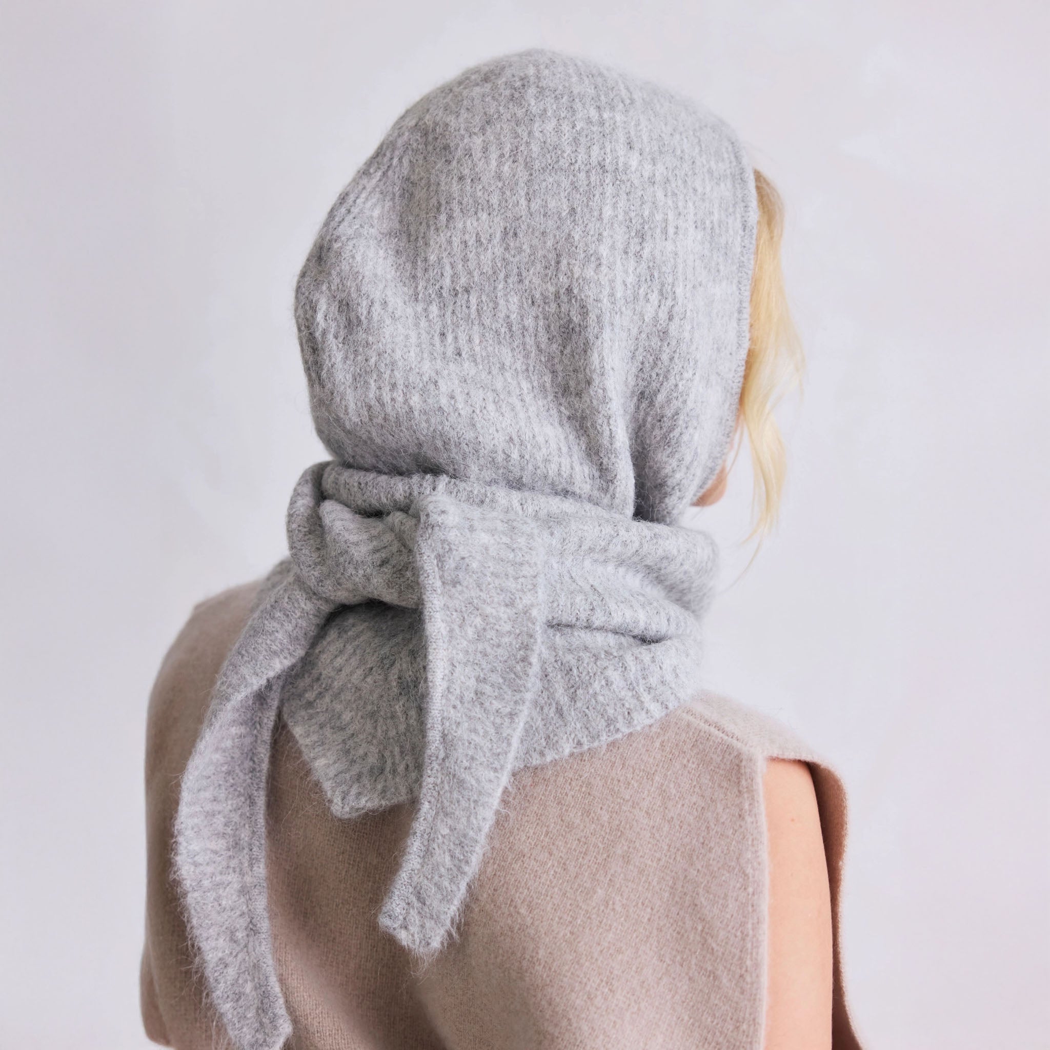 Person wearing a gray hooded knit scarf with a bow on a plain background