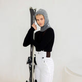 Person wearing a black sweater with a gray balaclava holding skis against a white background