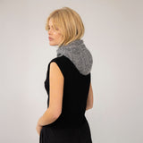 Woman wearing a black sleeveless top with a gray balaclavaf around her neck against a plain background