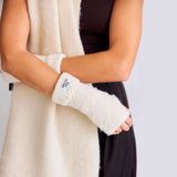 Person wearing  pebble beige fuzzy hand warmers with a visible brand label on a neutral background
