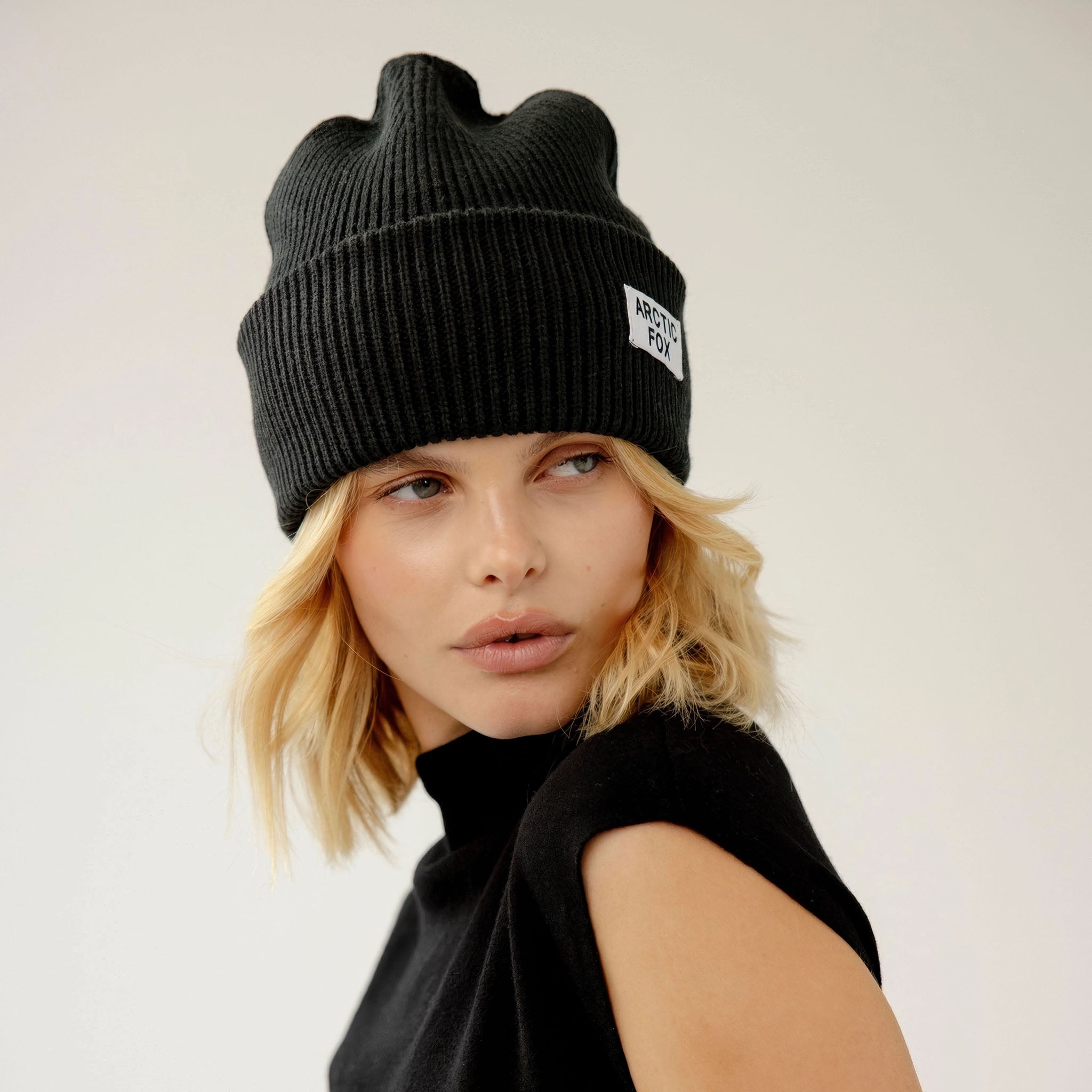 Model wearing a black knit beanie with an Arctic Fox logo on a plain background