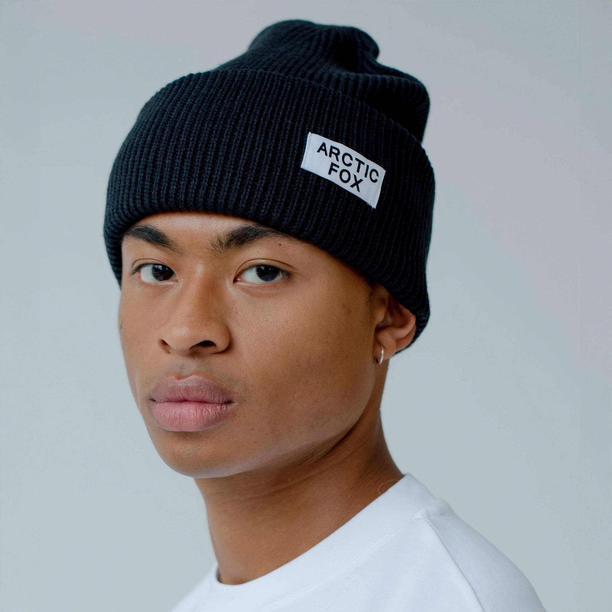 Model wearing a black knit beanie with 'Arctic Fox' logo against a plain background